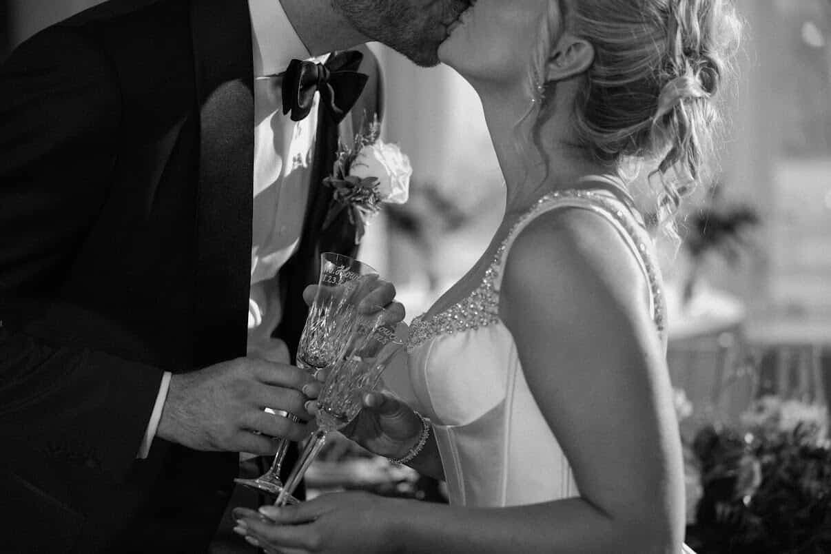Bride and groom kissing while holding their hand-engraved champagne flutes at a wedding in Baltimore, MD at The Belvedere.