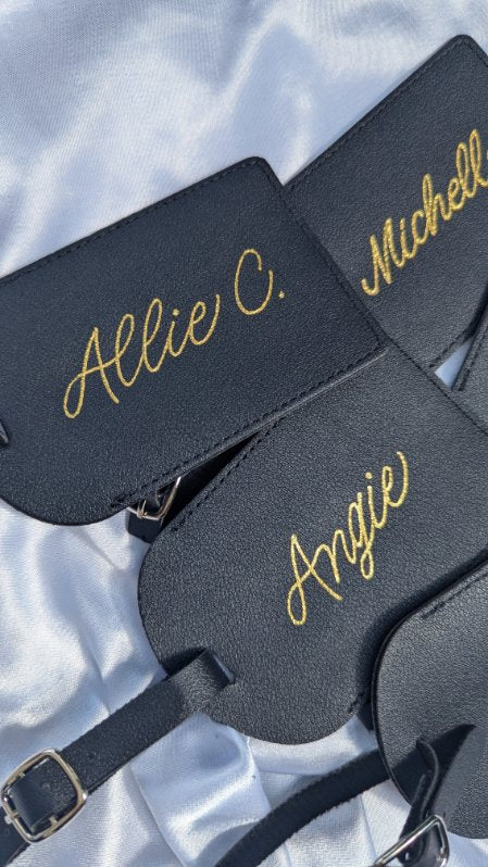 Black leather luggage tags hand heat foiled with gold fill, featuring personalized names “Allie C.” and “Angie.” Ideal for luxury brand activations, corporate gifting, and destination wedding favors.