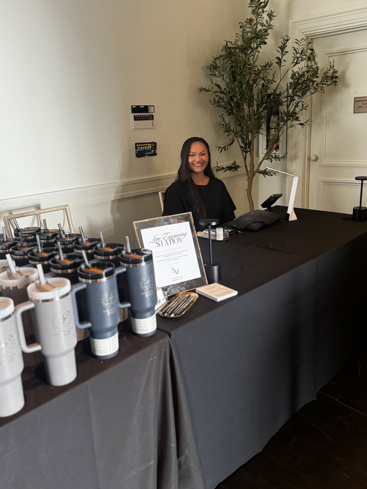 Tiffany of SLM & Design Co. performing live engraving on Stanley tumblers at a corporate event for Biogen at The Bellevue in Philadelphia, PA. On-site personalization setup for branded corporate gifting experience.