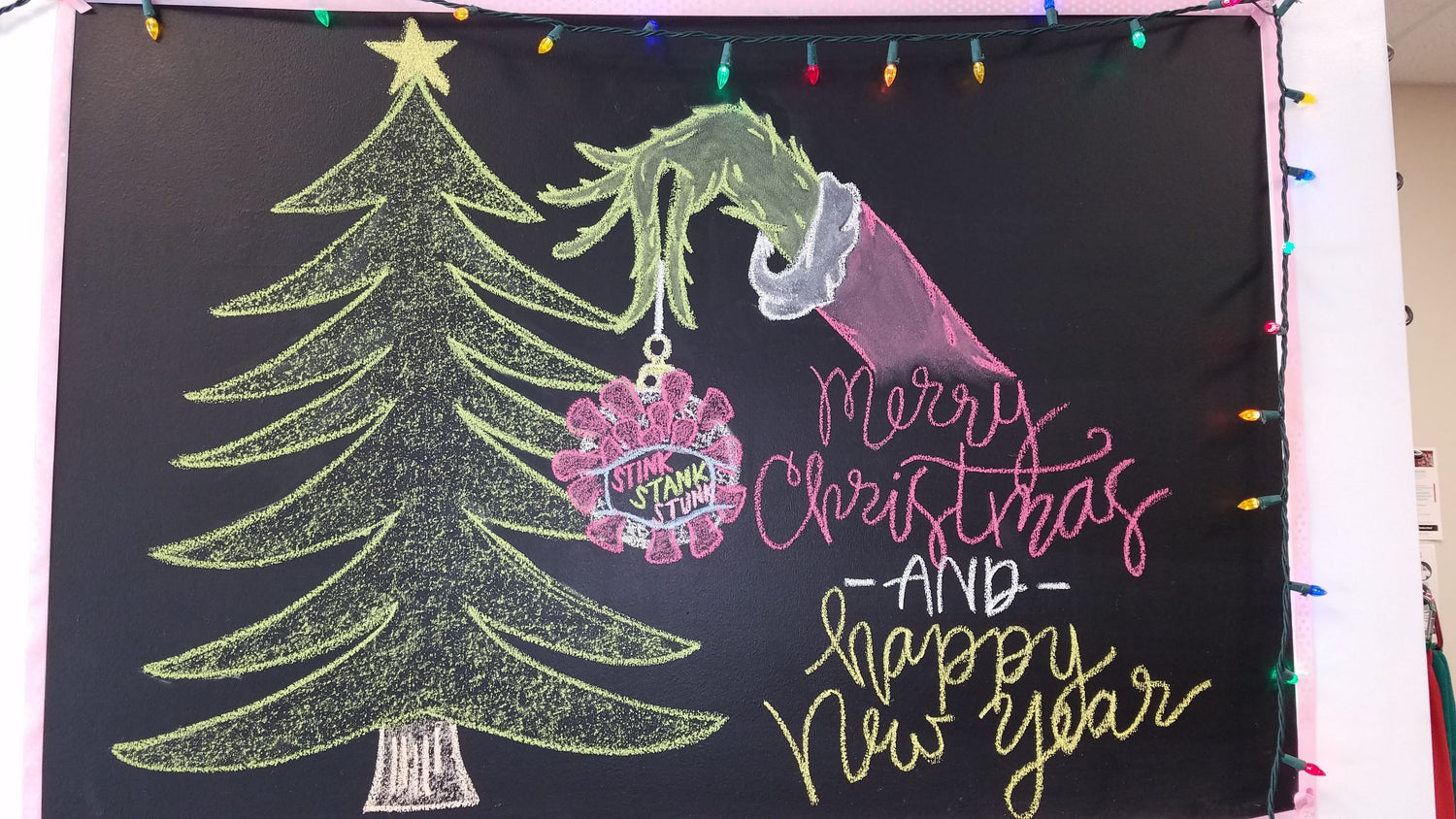 Grinch-themed Christmas chalkboard with coronavirus ornament, holiday tree, ‘Merry Christmas and Happy New Year’ text, and string lights at Select Physical Therapy in Carlisle, Pennsylvania