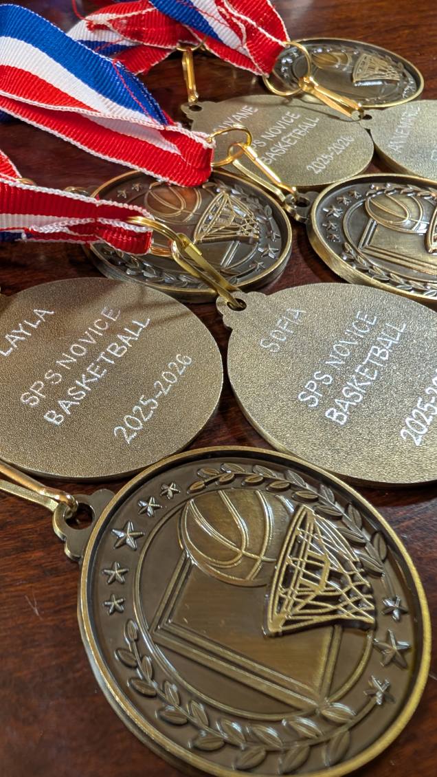 Hand engraved basketball medals for the Saint Patrick School Novice Girls Basketball Team (2025–2026 season), personalized with the names "Layla" and "Sofia" in Carlisle, PA. Custom sports awards created by SLM & Design Co. for a youth basketball celebration.