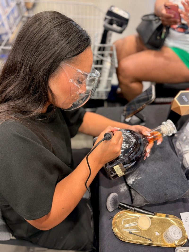 Tiffany of SLM & Design Co. performing live engraving on D'USSÉ Cognac bottles during a Father's Day weekend brand activation at Costco in Washington, DC. On-site bottle engraving for an interactive luxury brand experience.